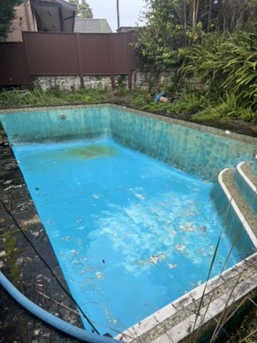 Pool partly cleared showing tiled walls and debris